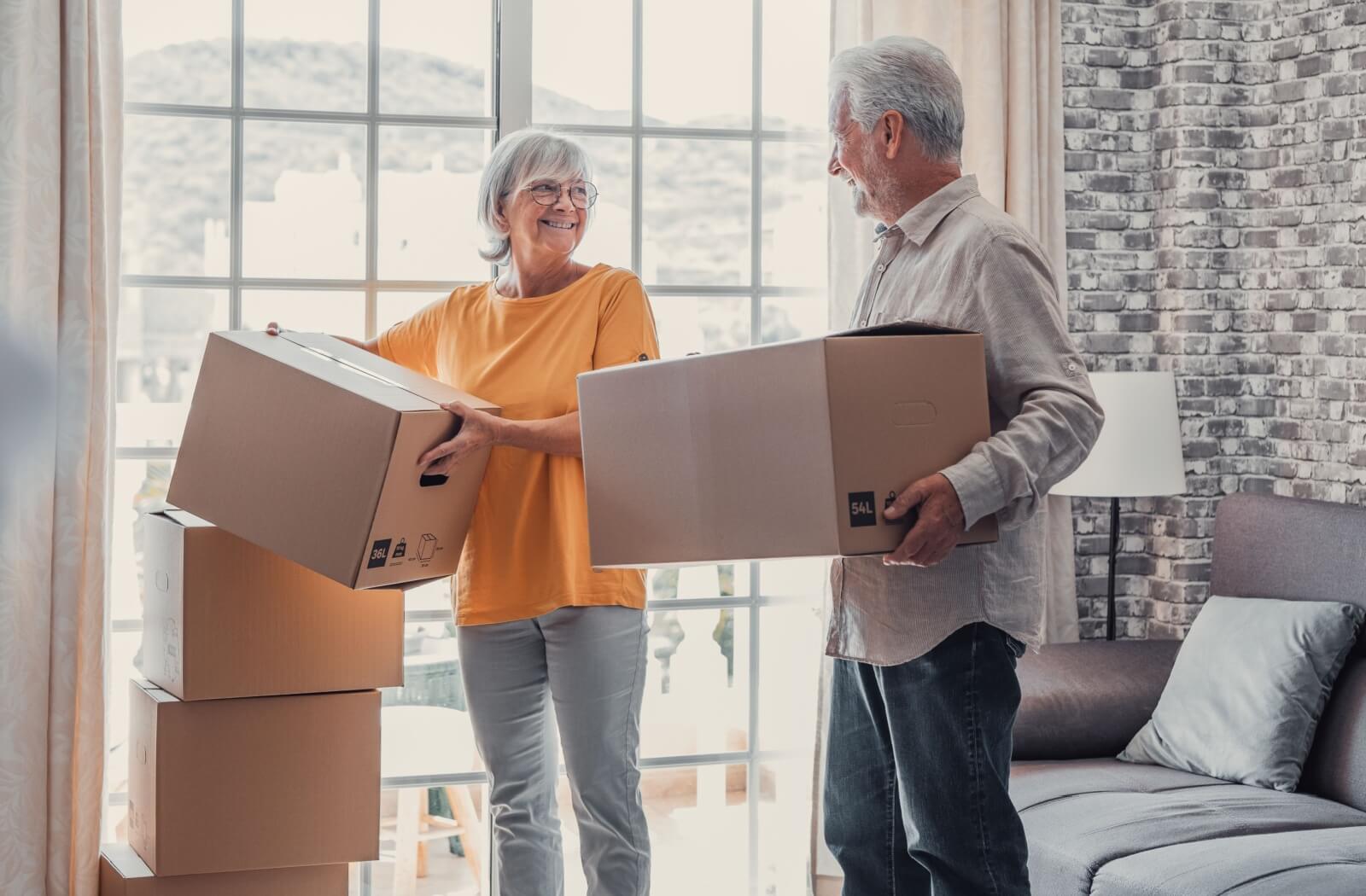 An older couple standing and smiling at each other while holding moving boxes