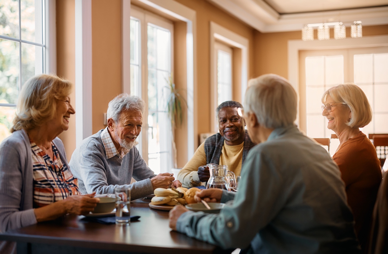 A group of older adults sitting around a table, eating and enjoying breakfast while smiling and chatting with each other.