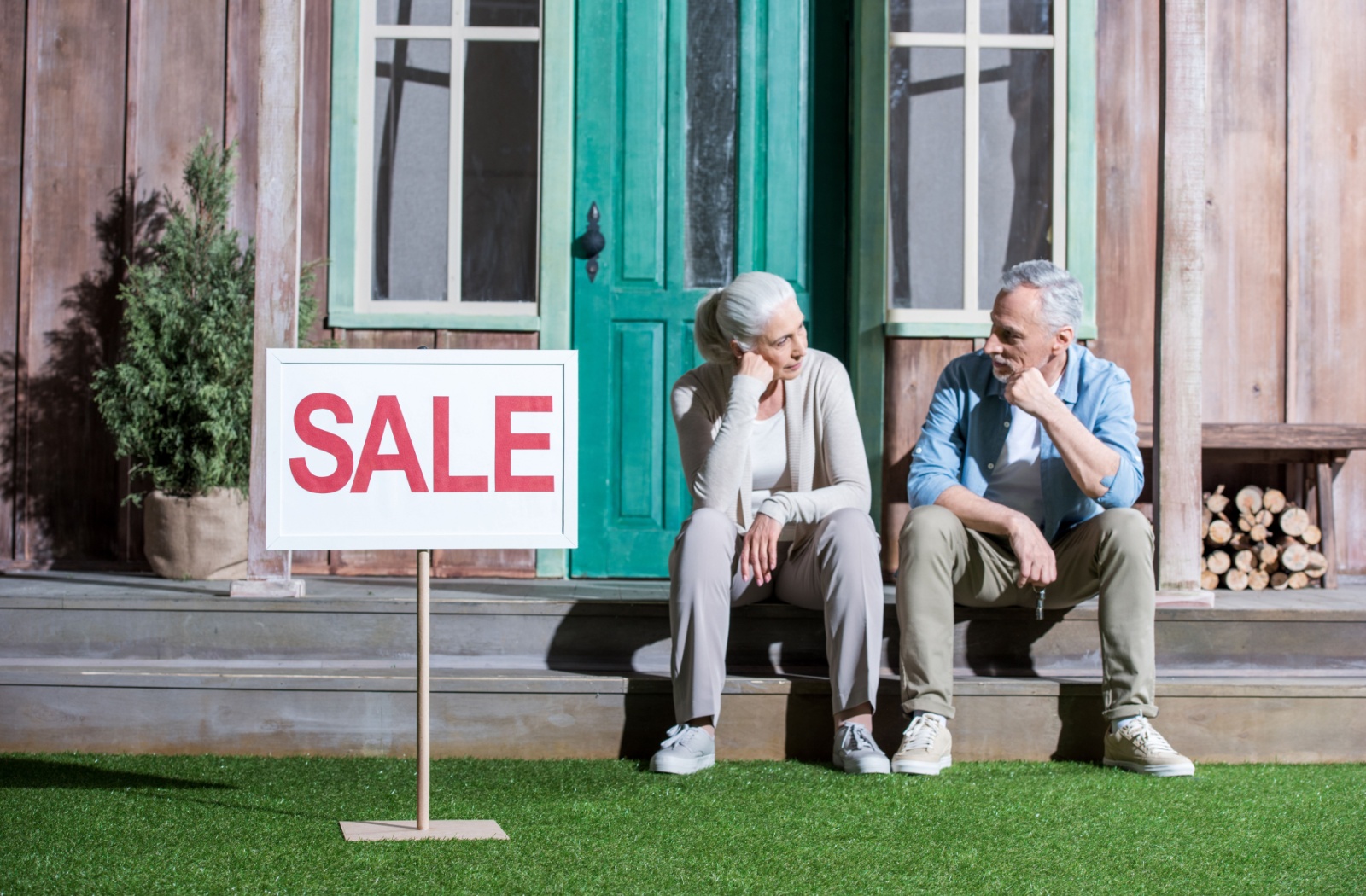 Two older adults sitting outside of their house that's for sale.