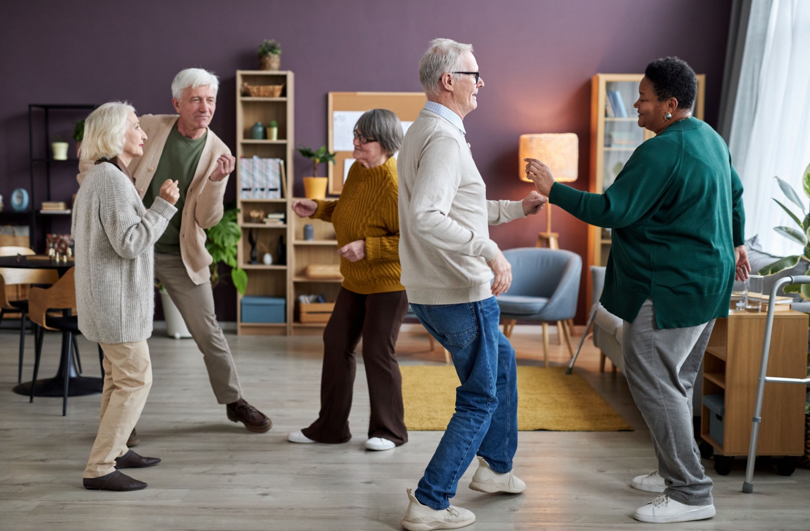 A group of happy seniors laughing and smiling together as they dance in their assisted living community's common area.