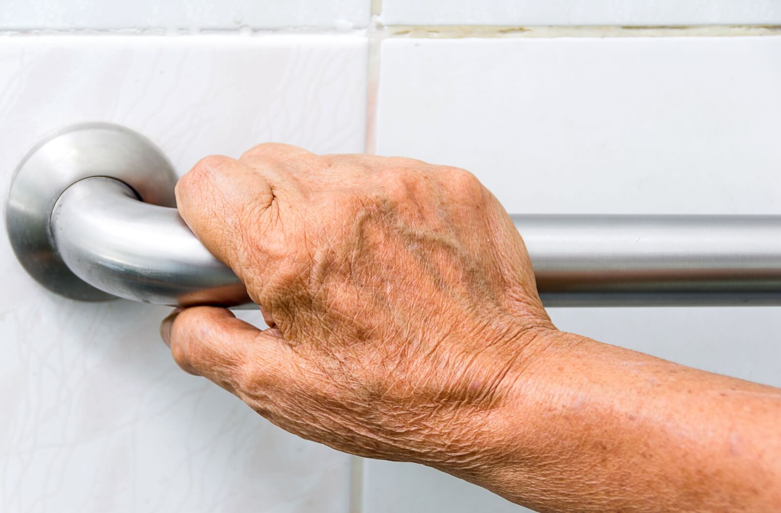 Close-up of a senior's hand holding onto a grab bar in a bathroom.