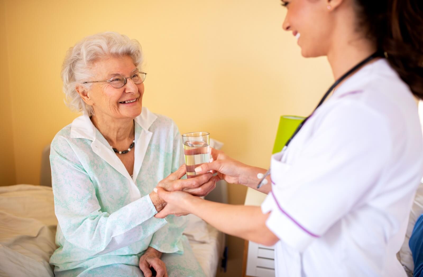 A happy resident in assisted living receiving a glass of water from a smiling staff member.