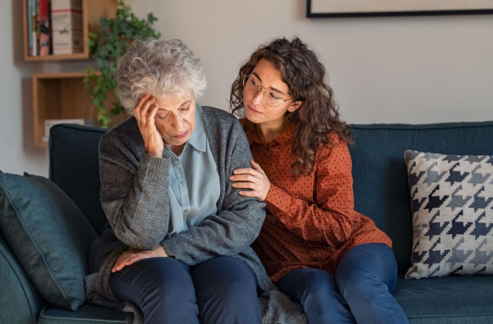 A person sitting on a couch consoles their elderly parent.