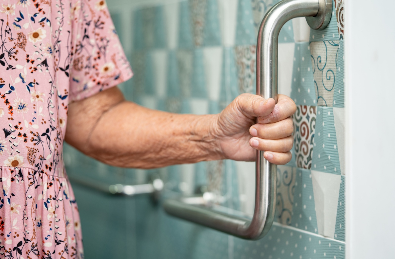 An older adult holds a grab bar in the bathroom of their assisted living home.