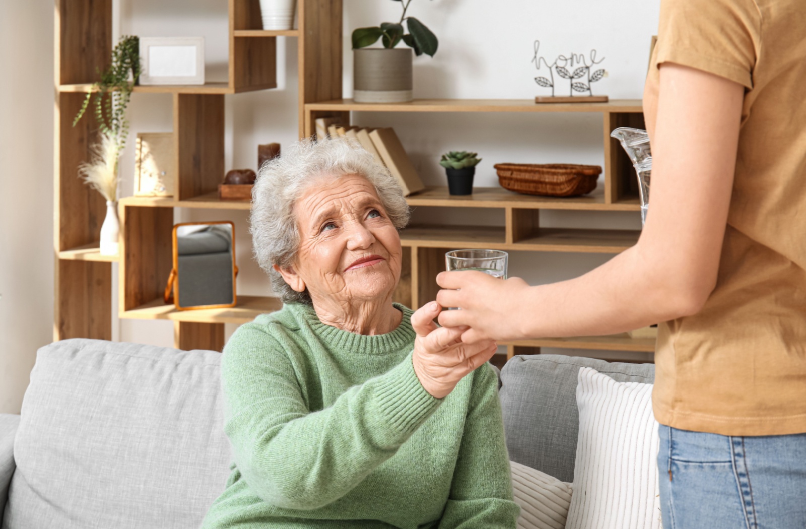 An older adult woman accepting a glass of water from her adult child.