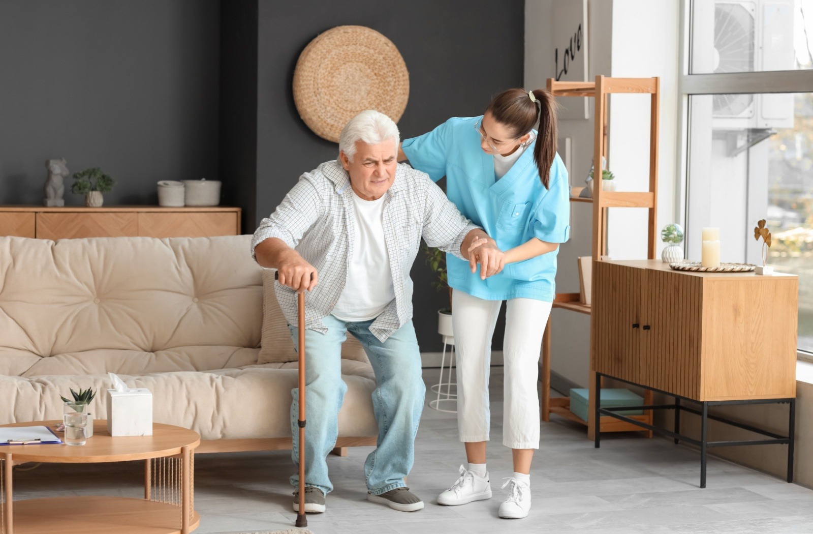 A female caregiver helping an elderly resident stand up from the couch he was sitting on.