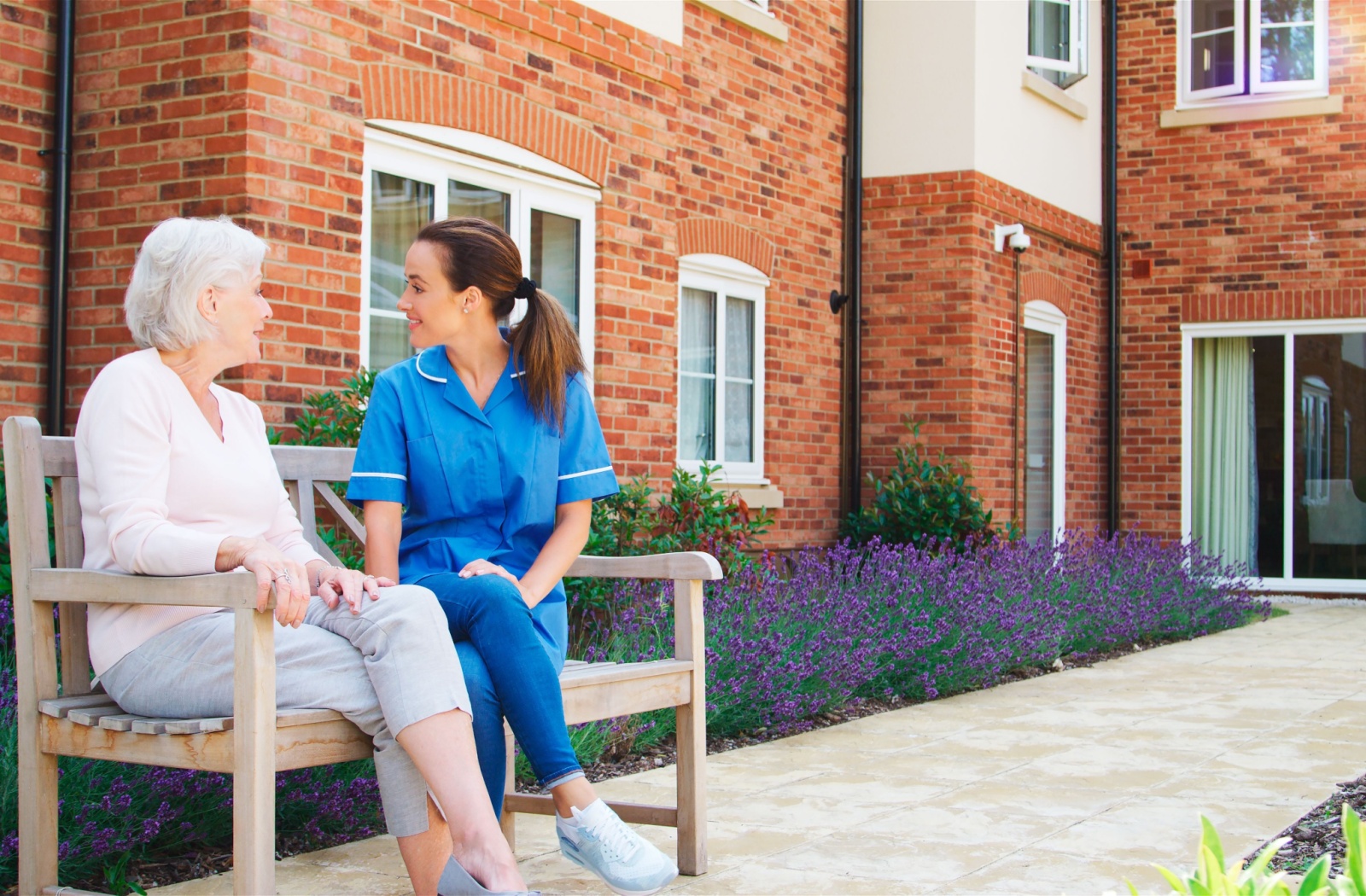 a caregiver sitting and chatting with a senior on a bench outdoors of senior living community